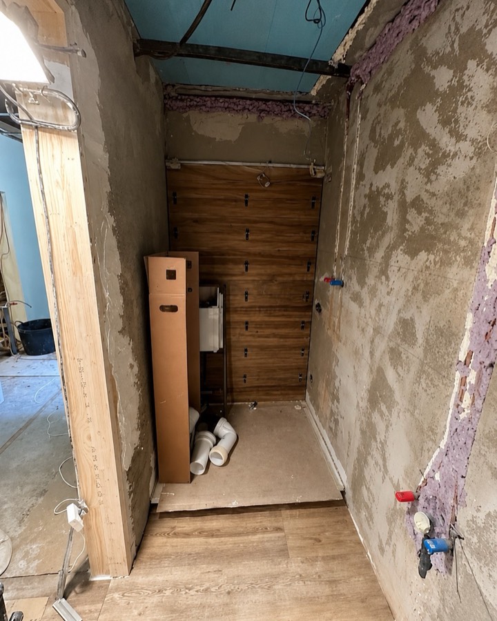 Baño desmontado hasta la obra, con las paredes picadas y las tuberías a la vista.