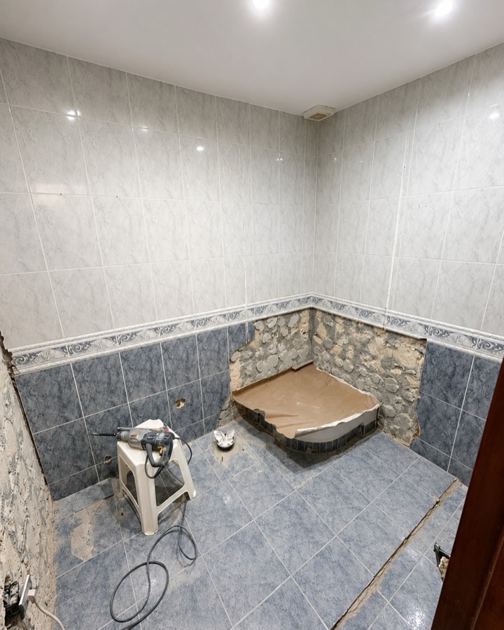 Baño antiguo alicatado en azul, con la bañera ya retirada y el hueco preparado.