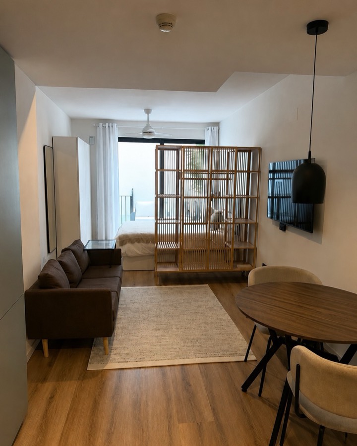 Dúplex amueblado con suelo de madera, sofá, mesa de comedor y estantería separadora.