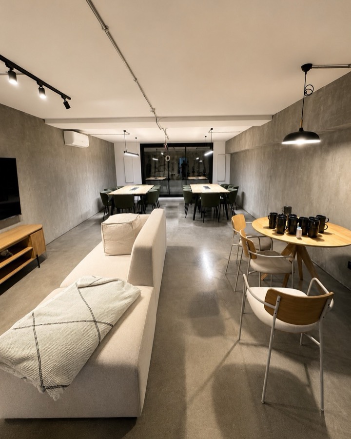 Coworking acabado en microcemento, con sofá, mesas de reunión e iluminación de raíl.