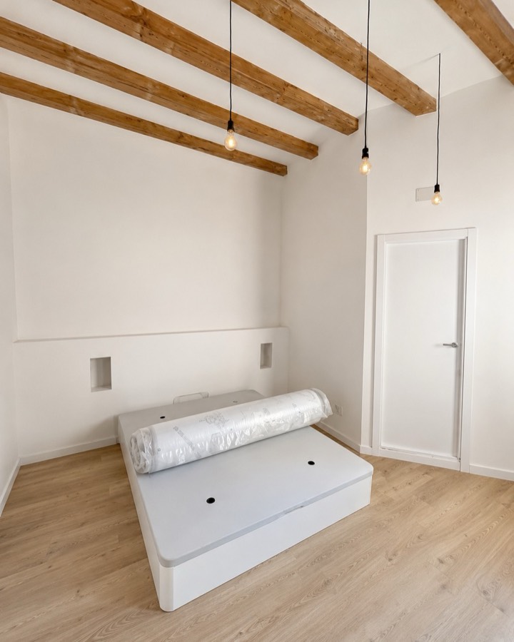 Dormitorio terminado en blanco, con las vigas de madera restauradas y suelo laminado.